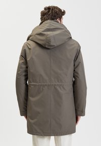 Parka grigia isolata con un ampio cappuccio, taglio dritto, vita elastica e senza chiusure visibili sul retro. Tessuto liscio e resistente all'acqua.