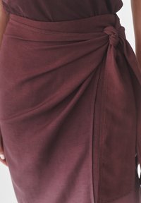 Bordeaux wikkelrok met een geknoopte strikdetail in de taille, gemaakt van zachte, gestructureerde stof en nette stiksels.