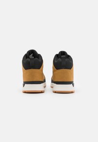 Zapatillas de deporte altas de ante marrón con acentos negros, cuello acolchado y suela blanca con un agarre de goma texturizada.