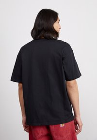 Juodas medvilnės marškinėliai su laisvu siluetu, trumpomis rankovėmis ir tiesiu kraštu. Išsiskiria paprastu dizainu ir sklandžia tekstūra.