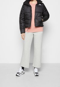 Veste matelassée noire avec un col montant, t-shirt rose, pantalon large gris clair, et baskets blanches avec des accents noirs. Textures lisses, style décontracté.