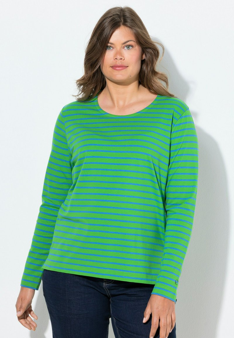 Vihreä pitkähihaisella paita, jossa on sinisiä vaakasuoria raidoja, pyöreä pääntie, pehmeä kangas ja rento istuvuus. Yhdistetty tummiin farkkuihin.