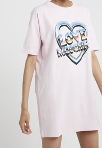 Růžové oversized tričko z bavlny s grafickým designem ve tvaru srdce a textem "LOVE MOSCHINO" v tučných, barevných písmenech.