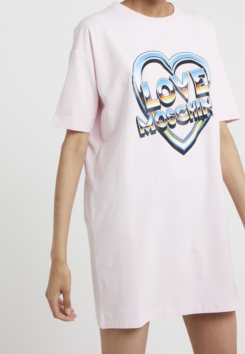 Růžové oversized tričko z bavlny s grafickým designem ve tvaru srdce a textem "LOVE MOSCHINO" v tučných, barevných písmenech.