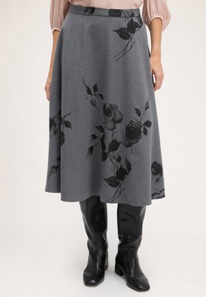 Jupe midi grise à imprimé floral noir associée à des bottes noires brillantes montant au genou et à un chemisier rose clair à manches bouffantes.
