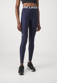 Mornarske plave tajice s širokim, bijelim pojasom s logotipom "Under Armour". Imaju glatku površinu i detalj s logotipom blizu gležnja.