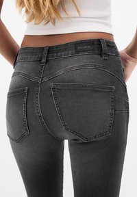 Jeans de mezclilla negra con un diseño ajustado, que presentan dos bolsillos traseros, detalles de costura sutiles y un logo de "PULL&BEAR" en la cinturilla.