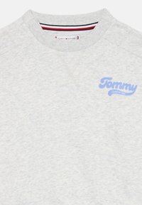 Grey cotton sweatshirt with ribbed crew neckline. Features blue "Tommy" logo on left chest, with red and white accents on the inner collar.