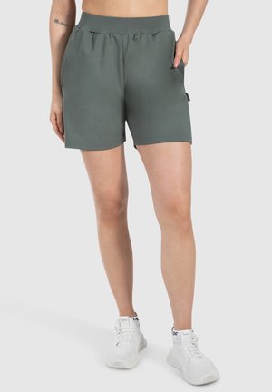 Groene sportshorts met een elastische tailleband, zijzakken en een gladde textuur, gecombineerd met witte sneakers.