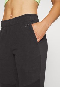 Zwarte fleece joggers met elastische tailleband, zijzakken en tonale logodetail. Zachte textuur en taps toelopend ontwerp voor comfort.