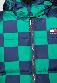 Puffer jacket in blue and green checkered pattern, featuring a zip closure, high collar, and logo patch on the chest. Smooth, shiny texture.