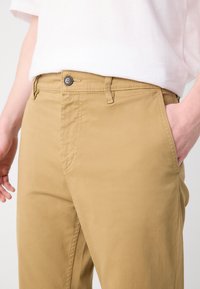 Kaki hlače s glatkom teksturom, ravnim krojem, pet džepova, zatvaračem i jednim dugmetom. Boja tan dopunjava ležernu odjeću.