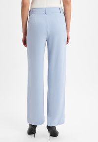 Lichtblauwe wijde pantalon van soepel stof, met een op maat gemaakte tailleband en plooidetails, gedragen met zwarte hoge hakken.