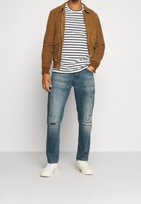 Brązowa zamszowa kurtka, biało-granatowa koszulka w paski, postarzane niebieskie dżinsy, białe trampki. Codzienny strój z kontrastującymi fakturami i kolorami.