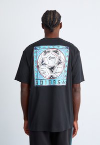 Sort bomulds T-shirt med et stort, multicolor grafisk tryk af en fodbold på ryggen, indrammet med dekorative accenter og tekst.