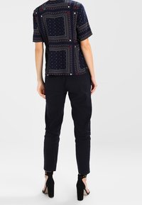 Camisa de patrón navy con mangas cortas, que presenta puntos y cuadrados blancos y rojos. Combinada con pantalones negros ajustados y zapatos de tacón.