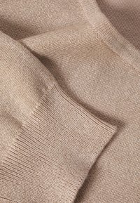 Svetlo bež pletena tkanina z gladko teksturo, z rebrastim manšetnim delom in diskretnim sijajem, ki poudarja udoben in moderen dizajn.