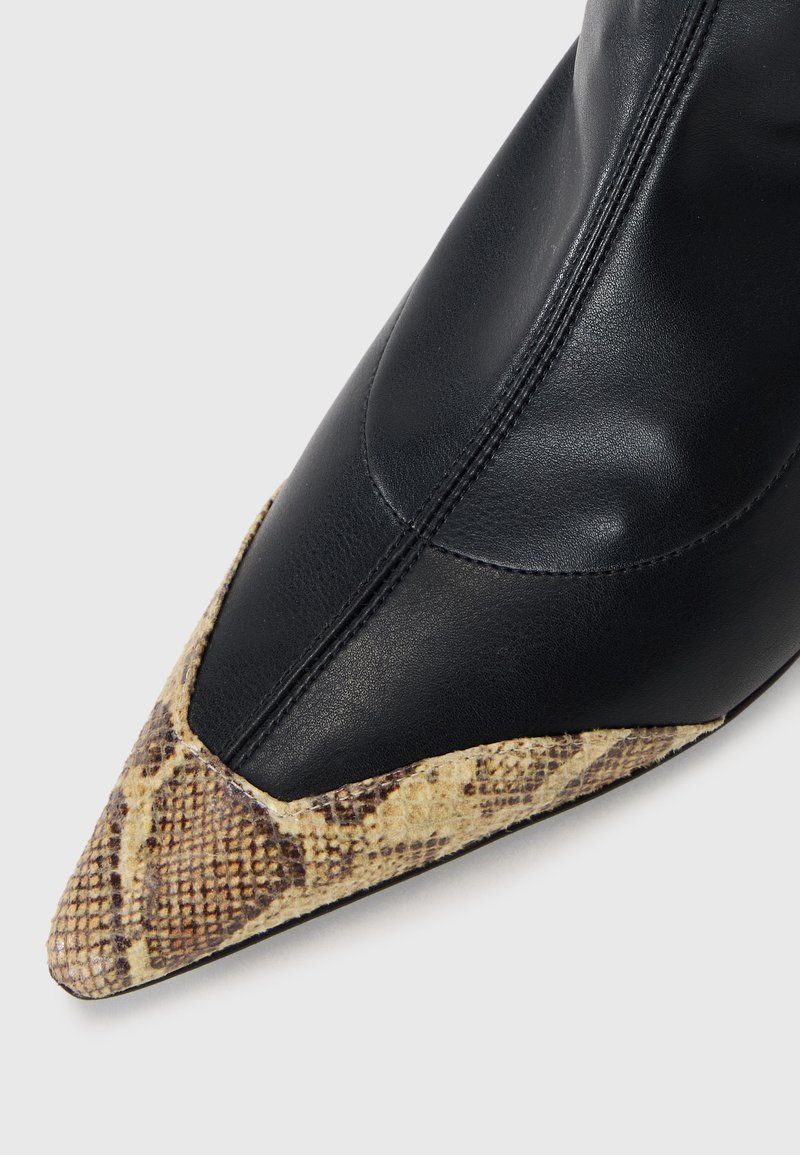Schwarze Lederstiefelette mit spitzem Zeh und einer strukturierten Schlangenhaut-Optik an der Vorderkappe in neutralen Farbtönen. Dezente Nähte sind entlang der Seiten sichtbar.