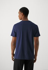 T-shirt en coton bleu marine avec un col ras du cou et des manches courtes, vu de dos. Texture lisse, coupe décontractée et design simple.