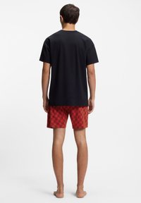 Melna kokvilnas T-krekls ar apaļu izgriezumu un īsām piedurknēm, saskaņots ar sarkaniem šortiem ar atkārtotu logotipa rakstu.