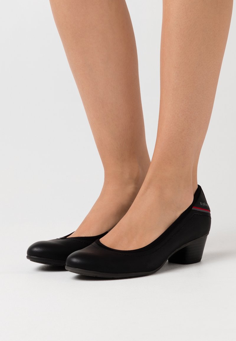 Escarpins à talon bas en similicuir noir avec bout arrondi et détail découpé sur le côté. Présentent un accent rouge subtil sur le talon et le logo.