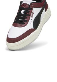 Fehér sneaker burgundi és fekete részletekkel, texturált bőrfelületekkel, fekete fűzővel és gumitalppal. Logó az oldalon.