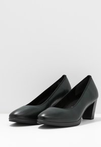 Pair of dark green leather mid-heel pumps with rounded toes, black stacked heels, and smooth finish on a white surface and background.