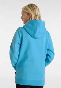 Modrá mikina s velkou nastavitelnou kapucí, dlouhými rukávy a volným střihem. Obsahuje malé logo na spodním lemu, vyrobená z měkké, texturované tkaniny.