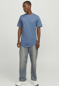 Blå bomulds t-shirt med korte ærmer, rund halsudskæring og lige snit, sammen med løse, falmede grå jeans og hvide sneakers.