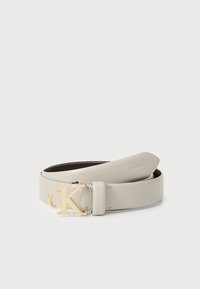 Cintura Calvin Klein in morbida pelle grigia. Presenta una fibbia logo in tonalità oro. Texture liscia con un design minimalista, estremità che si assottigliano delicatamente.