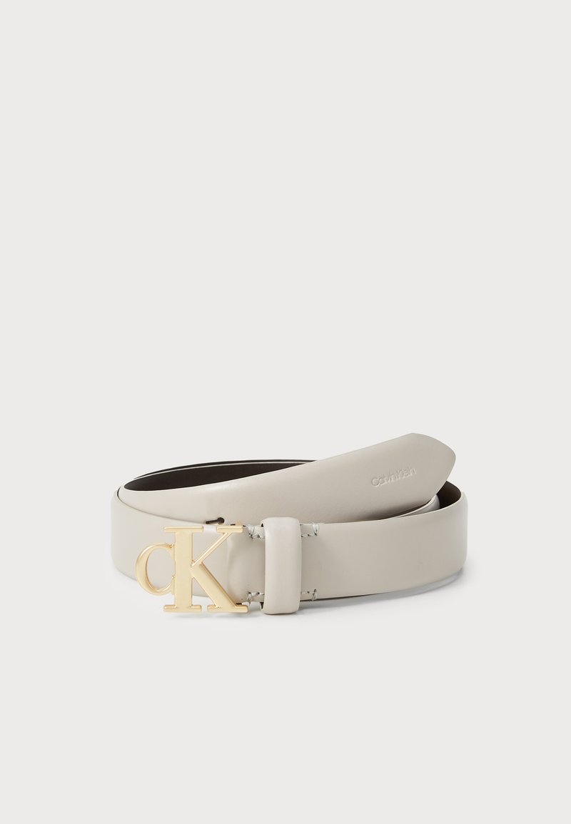 Cintura Calvin Klein in morbida pelle grigia. Presenta una fibbia logo in tonalità oro. Texture liscia con un design minimalista, estremità che si assottigliano delicatamente.