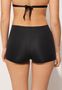 Černé plavky s hladkým, elastickým materiálem. Mají klasický střih a minimalistický design, vhodné na plavání nebo plážové nošení.
