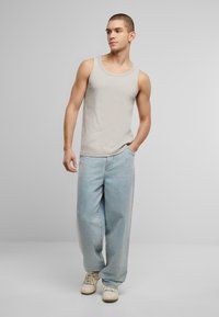 Lys grå tanktop med rund halsudskæring, parret med løstsiddende lyseblå denimjeans. Båret med hvide sneakers. Neutral baggrund.