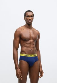 Ανδρικό εσώρουχο Nike σε ναυτικό μπλε με κίτρινη ζώνη μέσης με λογότυπο. Διαθέτει εφαρμογή που αγκαλιάζει και απαλό ύφασμα. Ομαλή υφή με ελάχιστα ραφές.