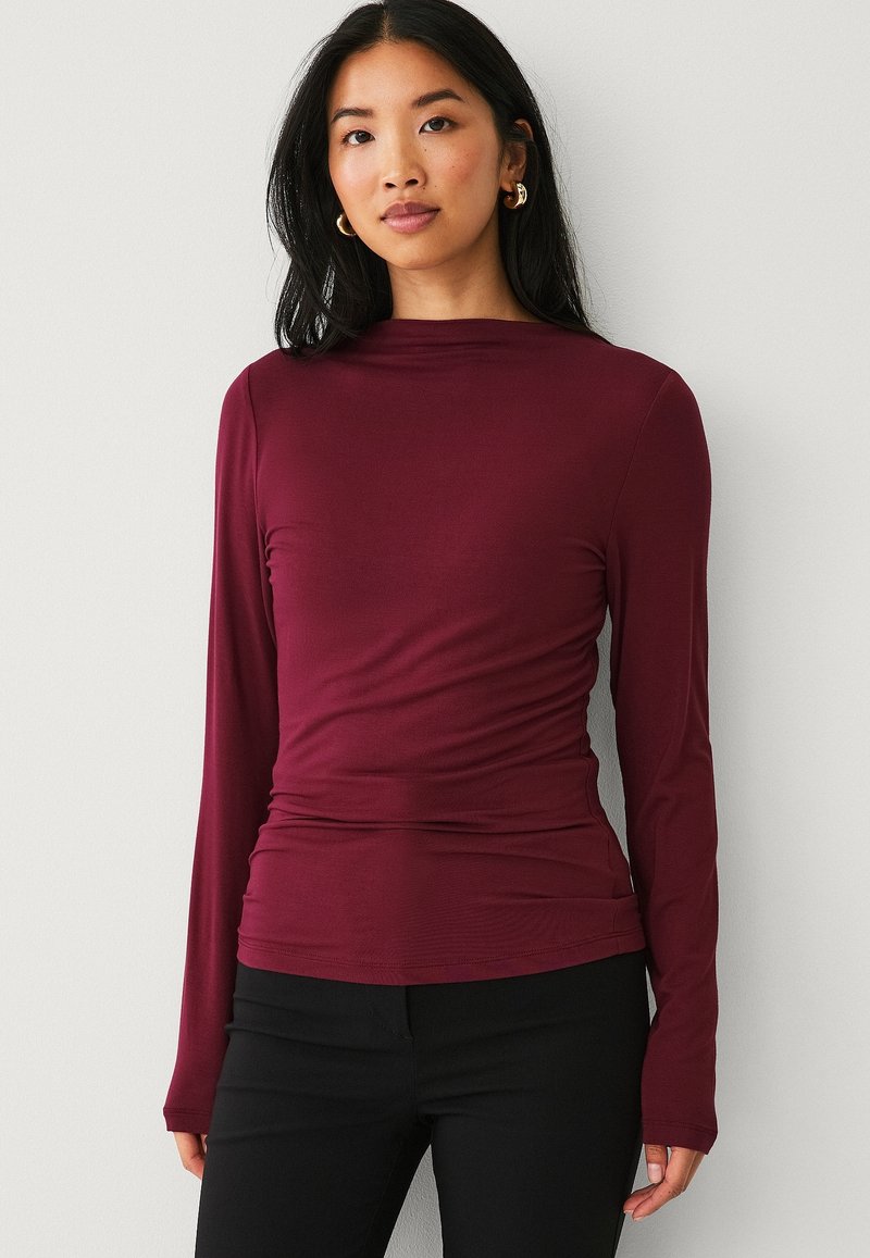 Bordeaux langemouw T-shirt met een getailleerde silhuet, zachte textuur en gerimpelde details bij de taille, gecombineerd met zwarte broek.