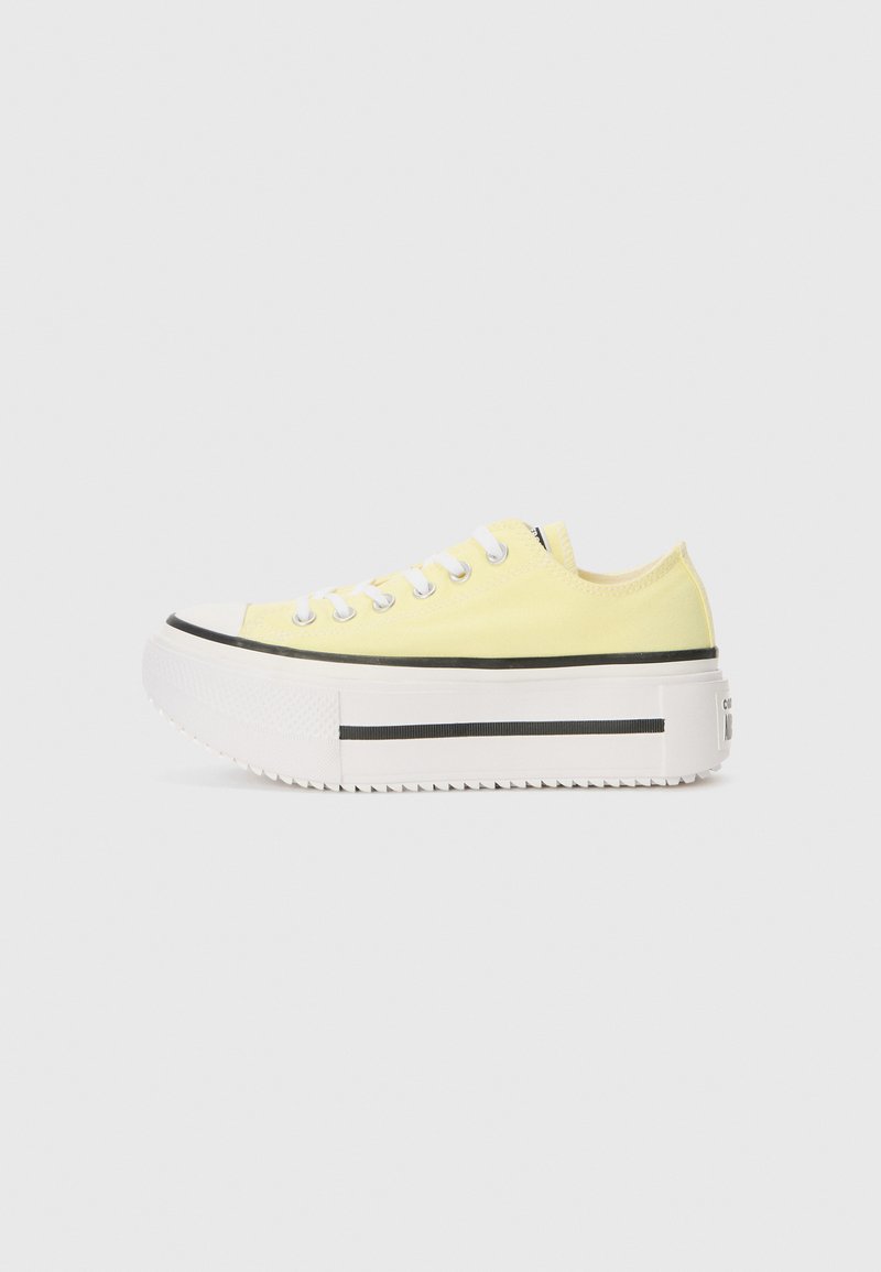 Yellow canvas sneakers with a white thick platform sole, black stripe, and round toe. Features white laces and a low-cut design.