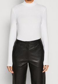 Weißer enger Rollkragenpullover mit langen Ärmeln, kombiniert mit hochtaillierten schwarzen Lederhosen, die eine glatte Textur und eine maßgeschneiderte Passform aufweisen.