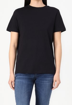 Czarny t-shirt z krótkim rękawem wykonany z bawełny, z okrągłym dekoltem i luźnym krojem. Ubrany z niebieskimi dżinsami.