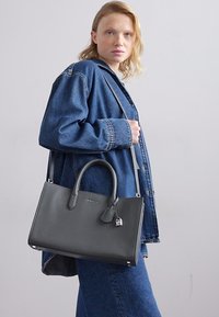 Bolso de cuero gris con asas dobles, forma rectangular, acentos de hardware menores, parte de un conjunto de denim casual sobre un fondo neutro.