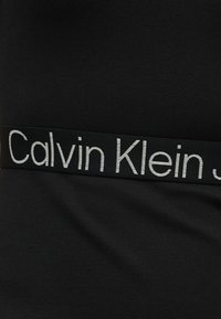Musta kangas, jossa musta joustava vyötärönauha ja osittain näkyvissä valkoiset "Calvin Klein"-tekstin kirjaimet.