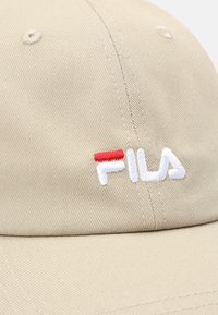 Gorra de béisbol beige con tejido acanalado, visera curvada y logotipo bordado "FILA" en blanco y rojo.