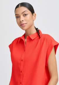 Camicia rossa a maniche corte con apertura a bottoni. Il tessuto presenta un motivo testurizzato e rigato, con colletto a punta e vestibilità comoda.