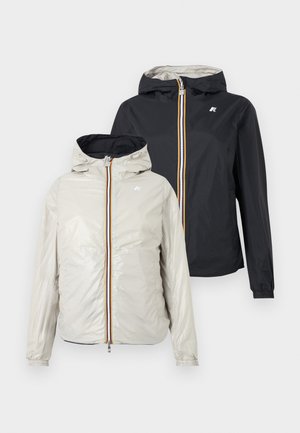 Δύο ελαφριές ζακέτες με κουκούλα και φερμουάρ μπροστά, μία σε ανοιχτό μπεζ και μία σε μαύρο, εμφανίζονται σε απλό φόντο.