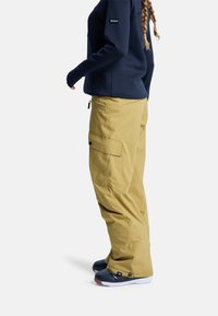 Žlté nepremokavé snehové nohavice s nákladnými vreckami a spevnenými lemami, v páre s tmavomodrým mikinovým vrchným dielom. Obsahujú logo na rukáve a priliehavý strih.