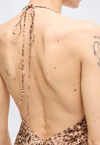 Άτομο με τοπ halter χωρίς πλάτη με λεοπάρ μοτίβο, με ορατές φακίδες και τατουάζ στην άνω πλάτη και τον ώμο.