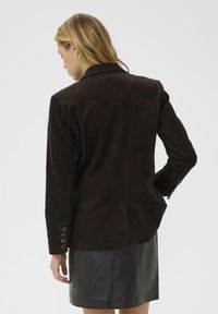 Ruskea corduroy-bleiseri, jossa on teksturoituja pystyraitoja, takana yksi halkio ja neljän napin hihadetaili. Päällä musta nahkahame.