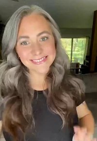 Kvinna med långt, vågigt grått hår, klädd i en svart skjorta. Mjuk belysning framhäver hennes drag mot en suddig inomhusbakgrund.