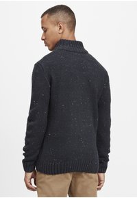 Marineblå strikket sweater med h�øj krave, prydet med farverige prikker og ribbede manchetter og kant. Vist fra bagsiden.