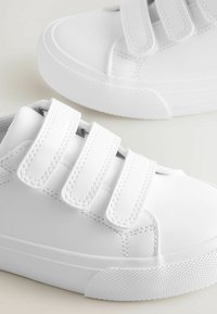 Vita sneakers med en slät syntetisk ovandel, tre justerbara kardborreband och en texturerad gummisula. Runtådesign.
