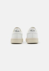 Hvite lær sneakers med en beige såle, med merket "VEJA" preget på hælen i grått. Glatt tekstur og rund form.